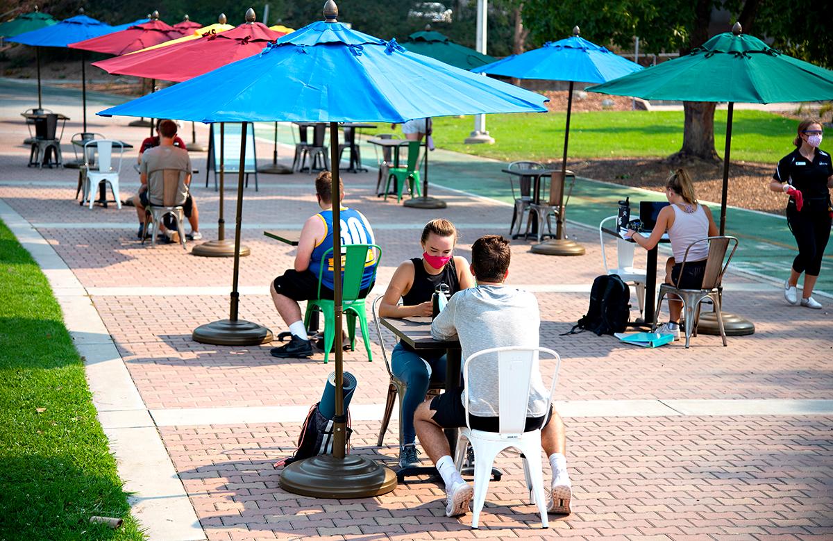Students sitting at tables with umbrellas