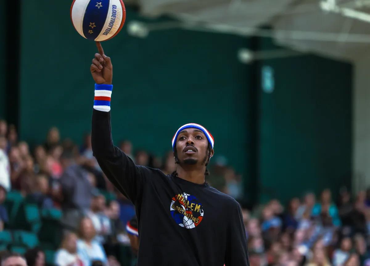 Basketball performer spins a Harlem Globetrotters ball on one finger during a live event in a crowded gymnasium.