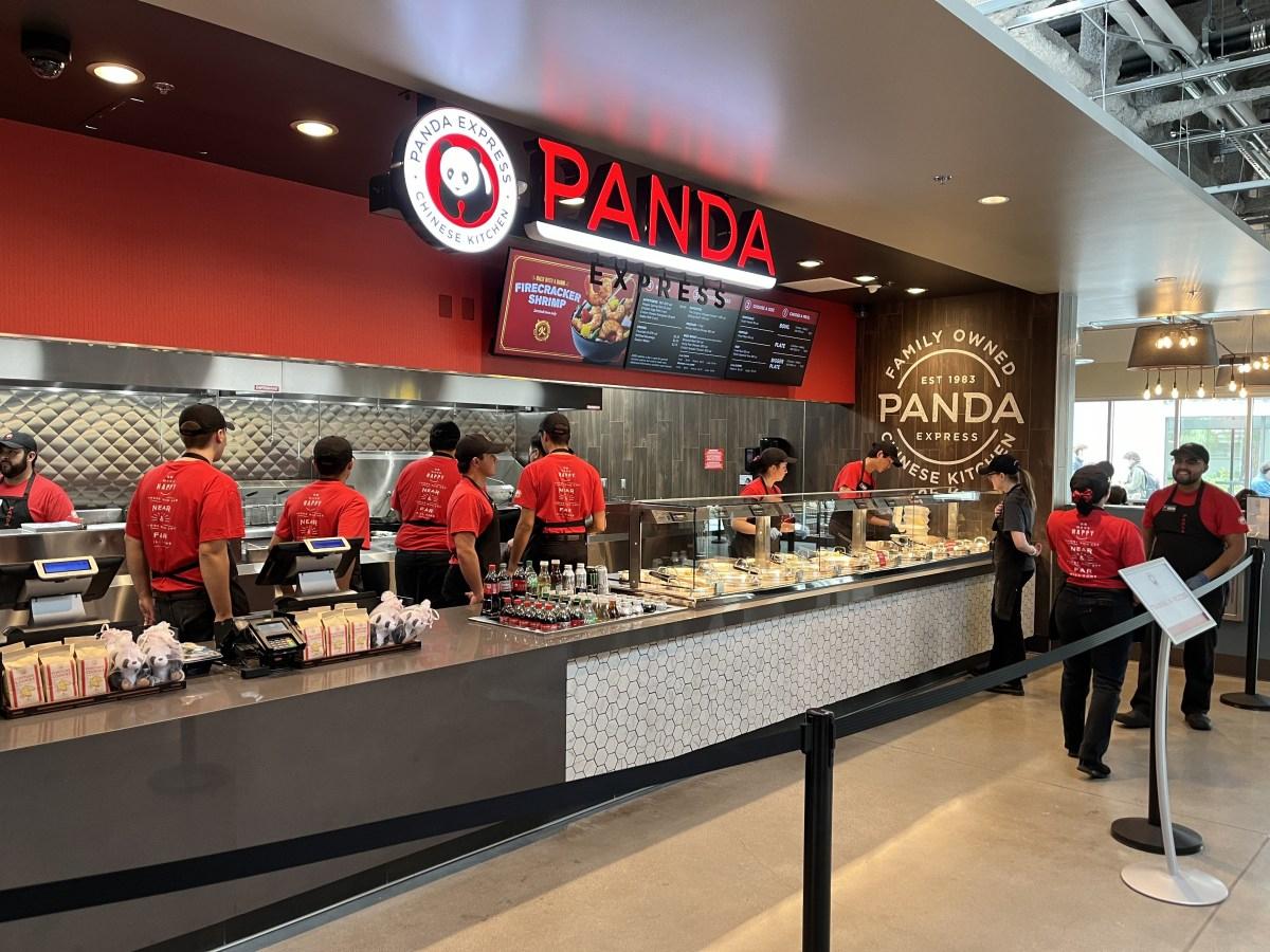 Employees work behind the counter at a Panda Express restaurant, preparing food for customers inside a modern dining area.