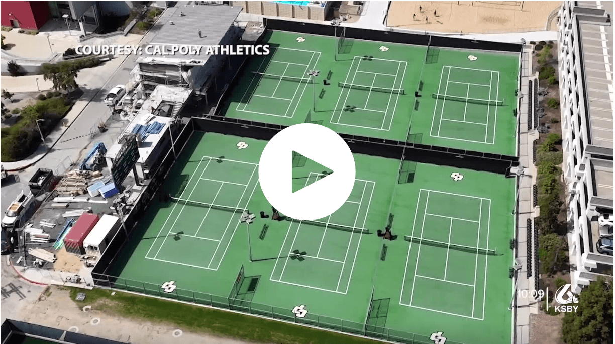 Aerial view of the Cal Poly tennis courts showing multiple green courts with white lines and Cal Poly logos, surrounded by fencing and nearby construction equipment, credited to Cal Poly Athletics.