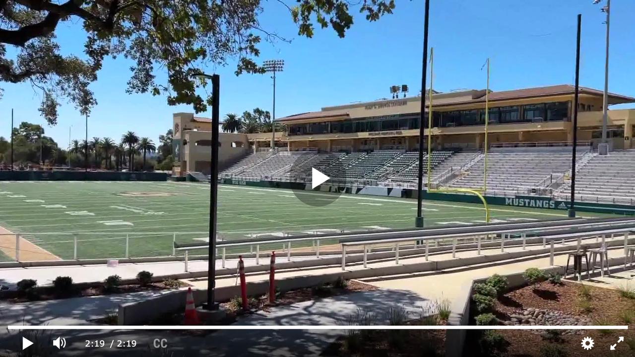 Wide view of Alex G. Spanos Stadium at Cal Poly on a sunny day, showing the football field, bleachers, and goalposts with “Mustangs” lettering visible in the end zone.