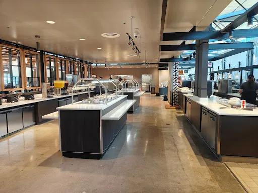 Spacious commercial kitchen and cafeteria area with modern stainless steel equipment, buffet stations, and polished concrete floors, located inside the Cal Poly dining facilities.