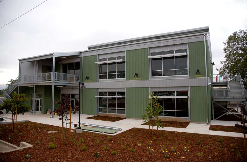 Exterior view of the Cal Poly Print and Copy building at the Tech Park, featuring a modern two-story green and gray structure with large windows.