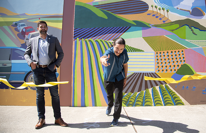 Muralist Oscar Pearson cuts the ribbon unveil a divided triptych wall at Via Carta on Cal Poly, San Luis Obispo's campus.