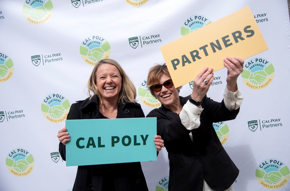 Two women holding up signs that read "Cal Poly Partners"